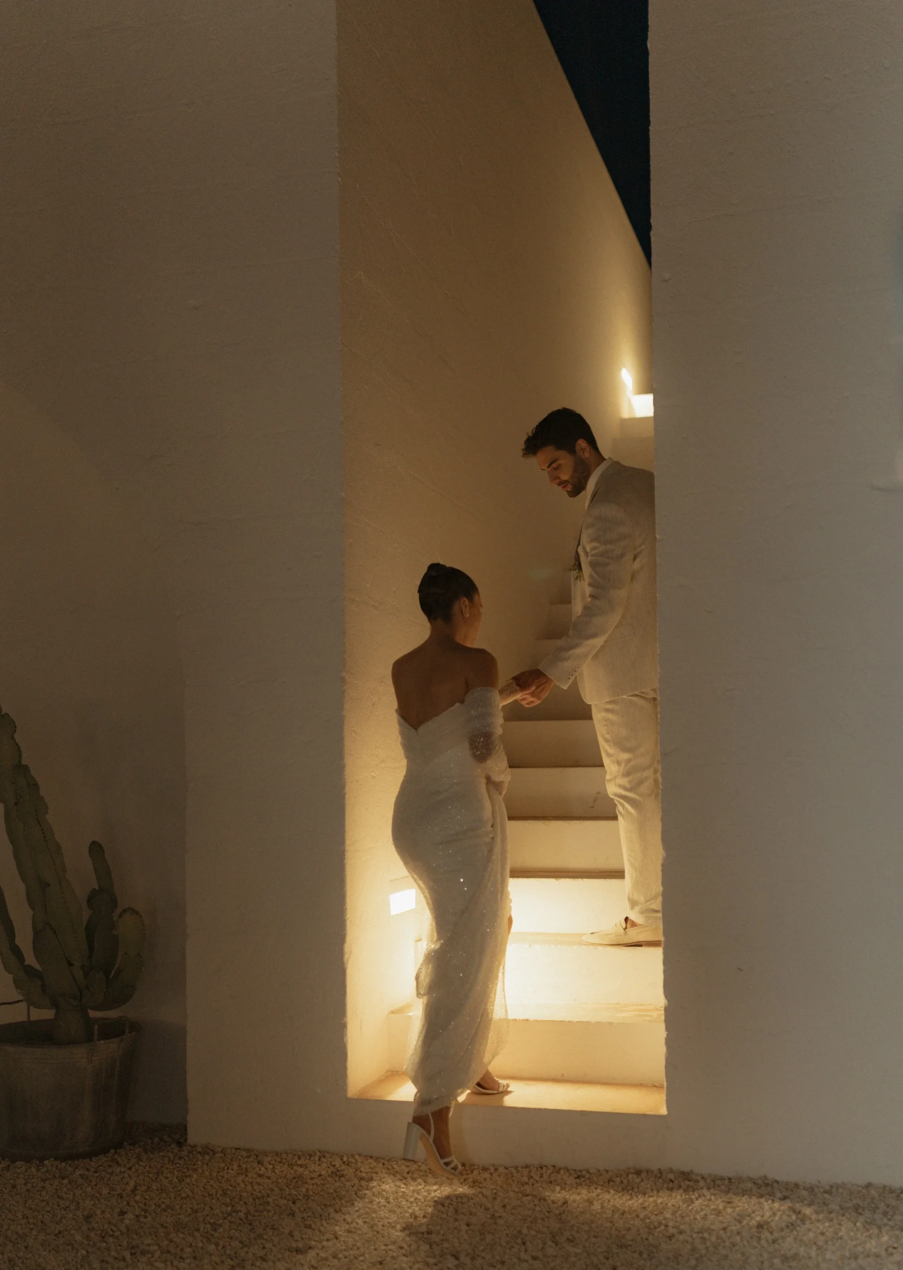 You pause halfway up the softly lit staircase at Masseria Moroseta, his hand reaching back for yours. The night is quiet except for the faint music drifting from the courtyard, and it feels like this moment belongs only to you.