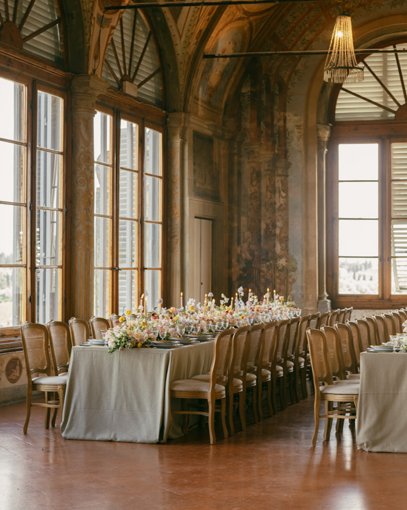 Reception table setup at Villa Corsini Florence with long banquet table, neutral linens, floral arrangements, and tall arched windows with natural light