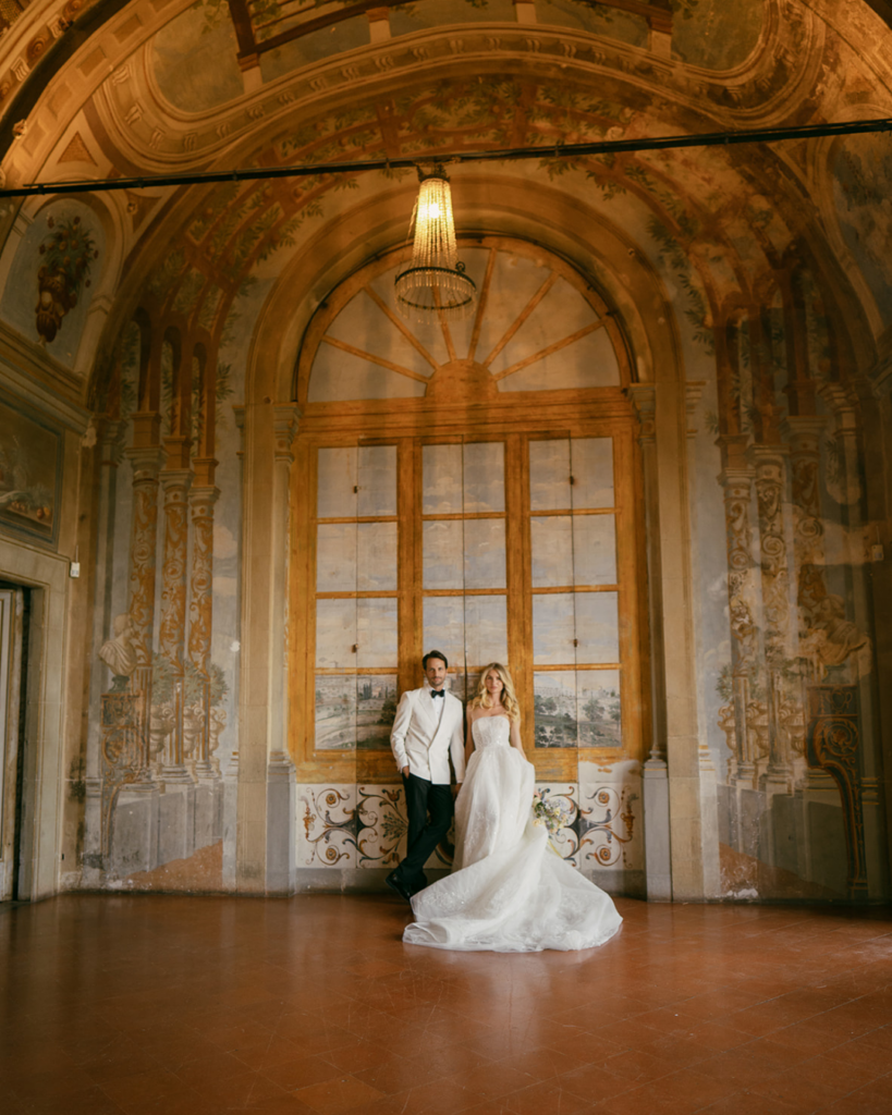 Bride and groom standing beneath frescoed ceiling and tall arched doors at Villa Corsini Florence with soft natural light and flowing wedding gown