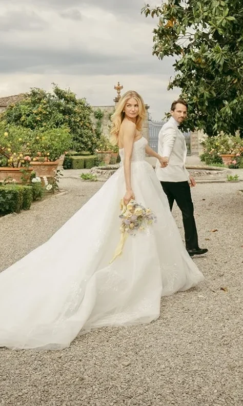 Bride in a flowing gown holding bouquet and groom’s hand while walking through the citrus gardens of Villa Corsini in Florence — captured by luxury film and digital wedding photographer Suzy Anderson.