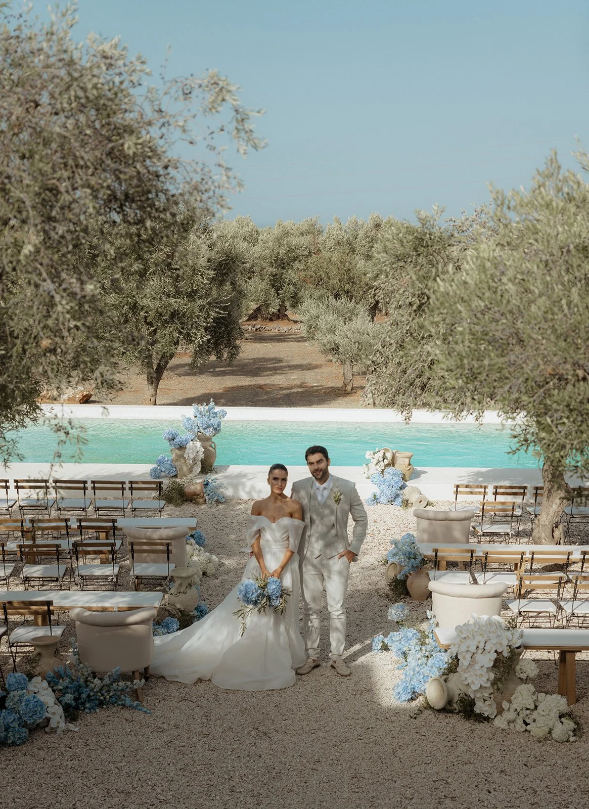 Bride and groom stand together in front of the ceremony location at Masseria Moroseta, framed by the rustic elegance of olive trees descending into the distance, creating a stunning natural backdrop for their wedding.