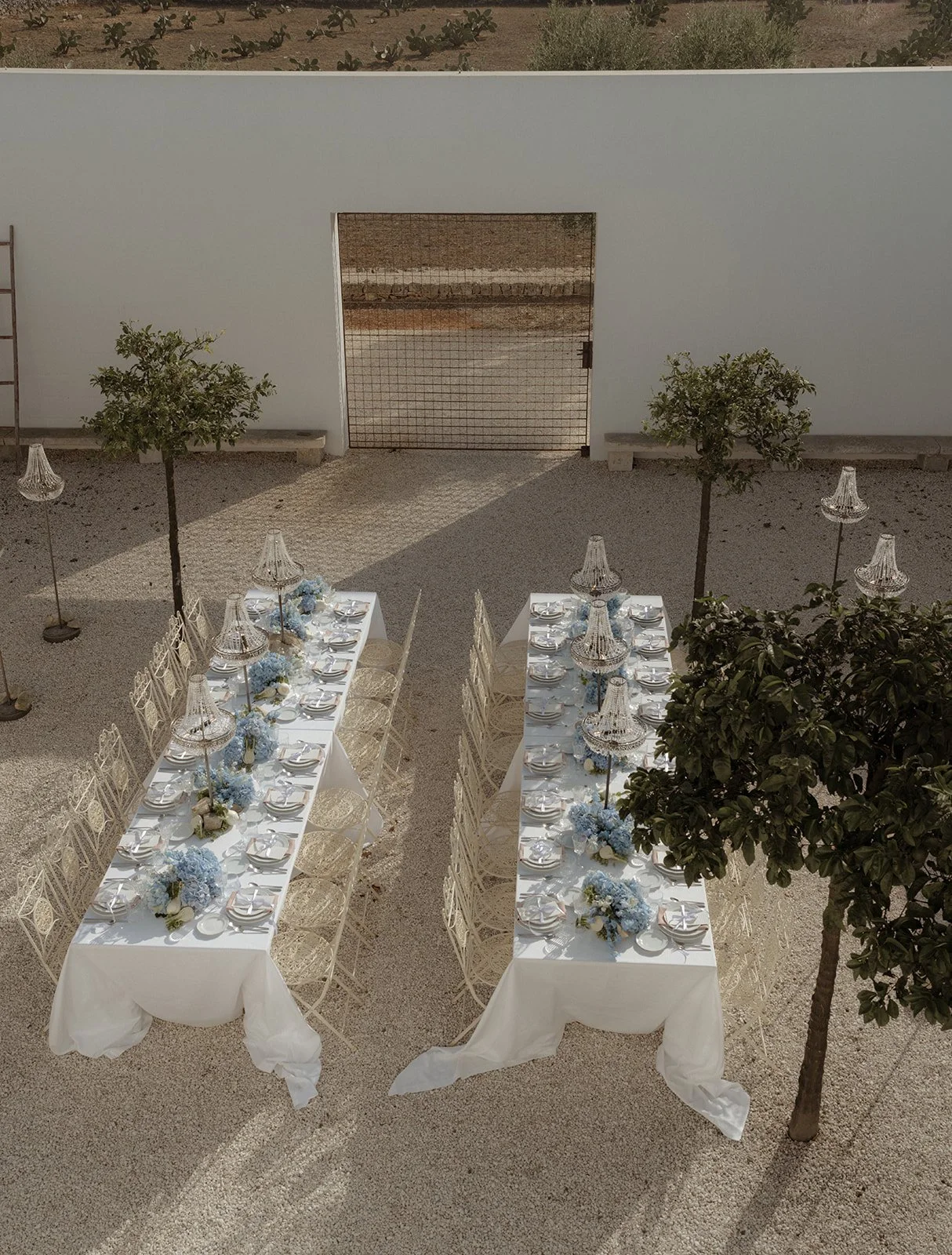 Aerial view of the dinner reception at Masseria Moroseta, styled by Mae& Co Creative, featuring long tables adorned with elegant florals and illuminated by stunning chandelier lamps, with a striking cactus-filled field serving as the backdrop.