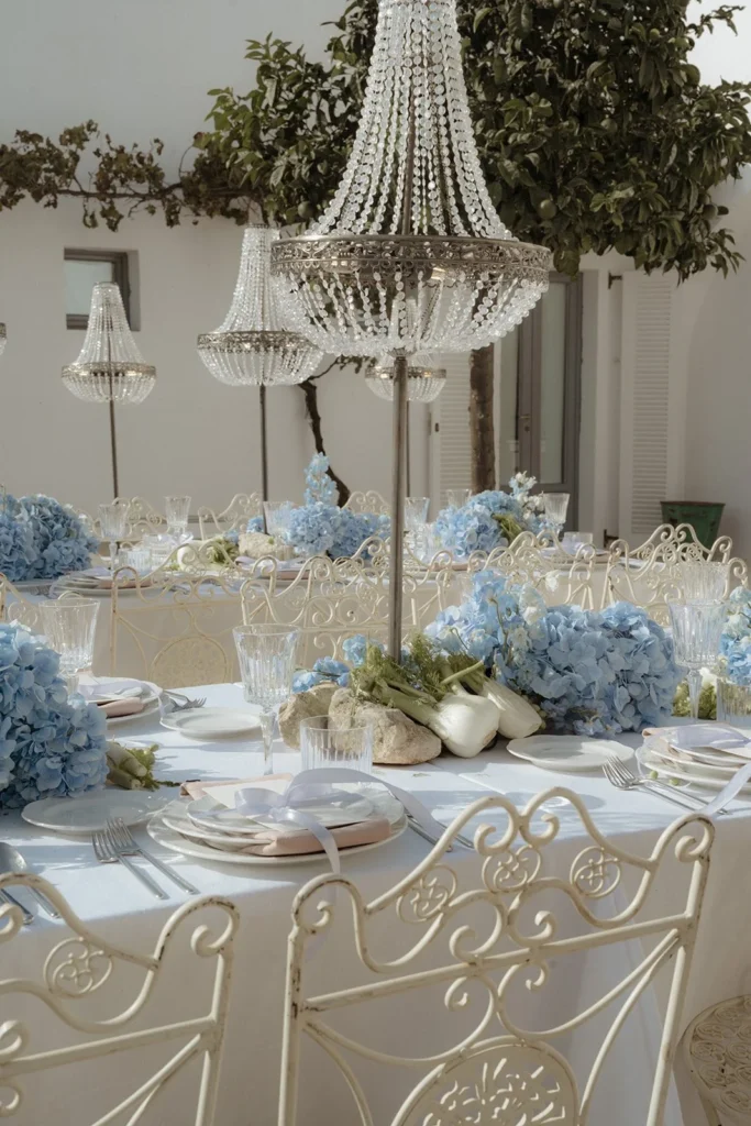 Outdoor wedding reception table with blue hydrangea florals, crystal chandeliers, and elegant place settings at Masseria Moroseta in Puglia, Italy.