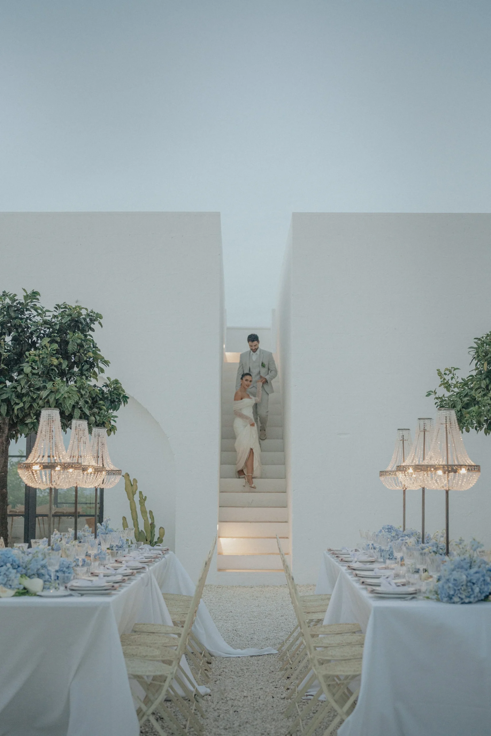 Bride and groom descend the iconic white stone stairwell at Masseria Moroseta, with the bride wearing a sleek, modern Eva Lendel gown, embodying effortless elegance in the heart of Puglia.