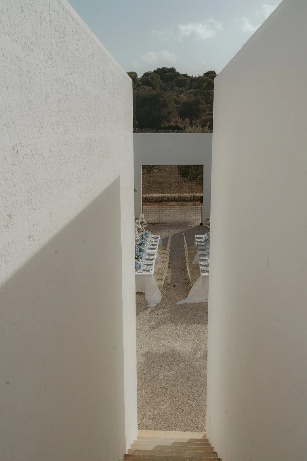 A photographer’s perspective from within the iconic stairwell at Masseria Moroseta, capturing the elegantly designed dinner reception area below, styled by Mae& Co Creative, with soft lighting and sophisticated decor creating a magical atmosphere.