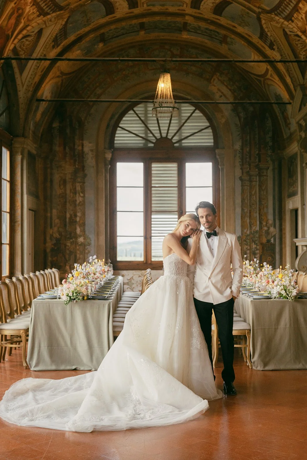   A stunning couple standing elegantly in front of a beautifully designed tablescape at    Villa Corsini   , crafted by    Kaleb Norman James.    The exquisite design features luxurious florals by    Winsome Floral   , complementing the romantic ambiance of the venue. The couple’s attire perfectly aligns with the sophisticated atmosphere, as soft candlelight illuminates the intricate table setting. Designed by    NKT Events,    the scene is a seamless blend of timeless beauty and modern elegance, capturing the essence of their love and the stunning surroundings.  