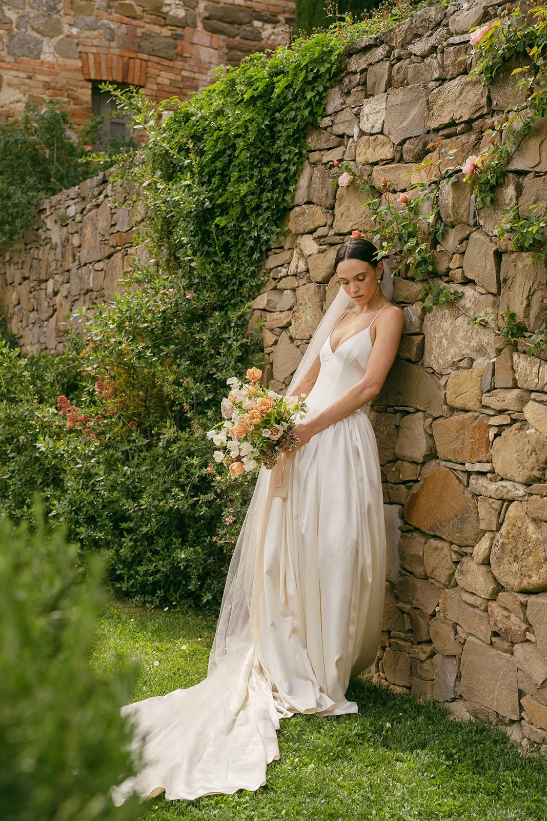   A bride exudes modern elegance in a sleek    Danielle Frankel gown   , standing against the breathtaking backdrop of    Monteverdi Tuscany   . The gown’s contemporary silhouette beautifully contrasts with the historic charm of the venue’s stone architecture and rolling countryside views. She holds a refined bouquet by    Winsome Floral,    featuring delicate blooms that complement the natural tones of the Tuscan landscape. The soft, golden light enhances the romantic yet sophisticated ambiance, capturing the essence of a timeless yet modern wedding aesthetic.  