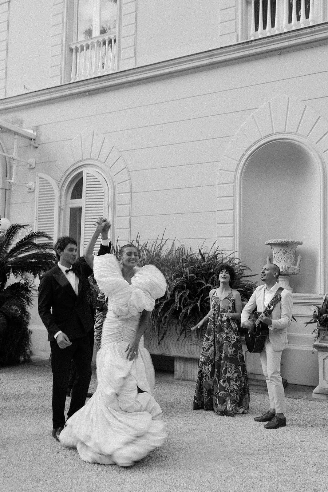  A black-and-white image with a slight motion blur, capturing the groom twirling his bride on the dance floor. The musicians, Jamin the Jukebox, are softly visible in the background, adding to the energy and emotion of the moment. It’s raw, alive, and full of movement—like a beautiful, fleeting memory.   