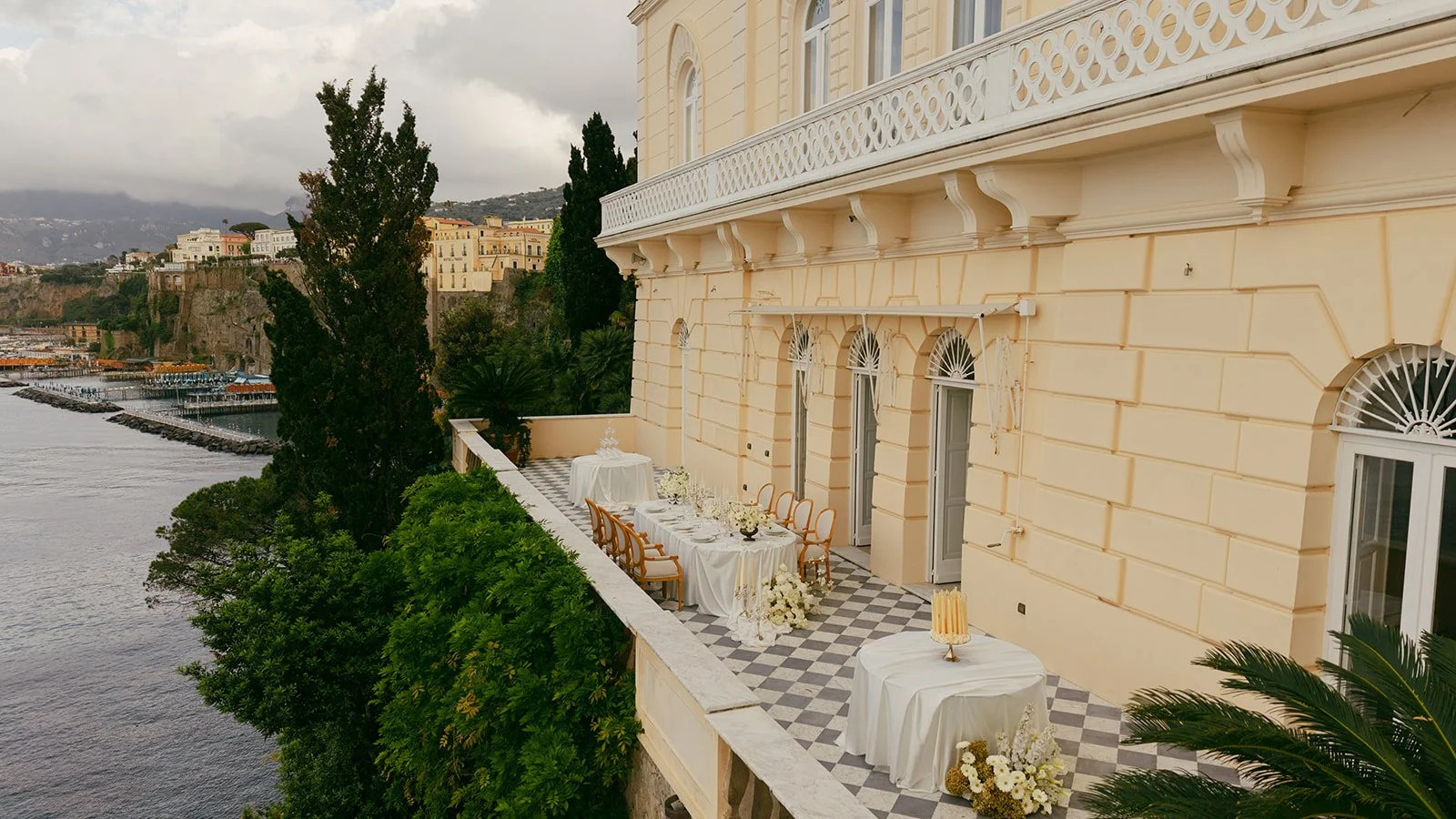  A drone view from the side of the dinner reception on the iconic balcony at Villa Astor. The tables are set perfectly, and beyond the railing, you can see the harbor of Sorrento stretching out below. The scene feels open and inviting—where celebration meets breathtaking views. 