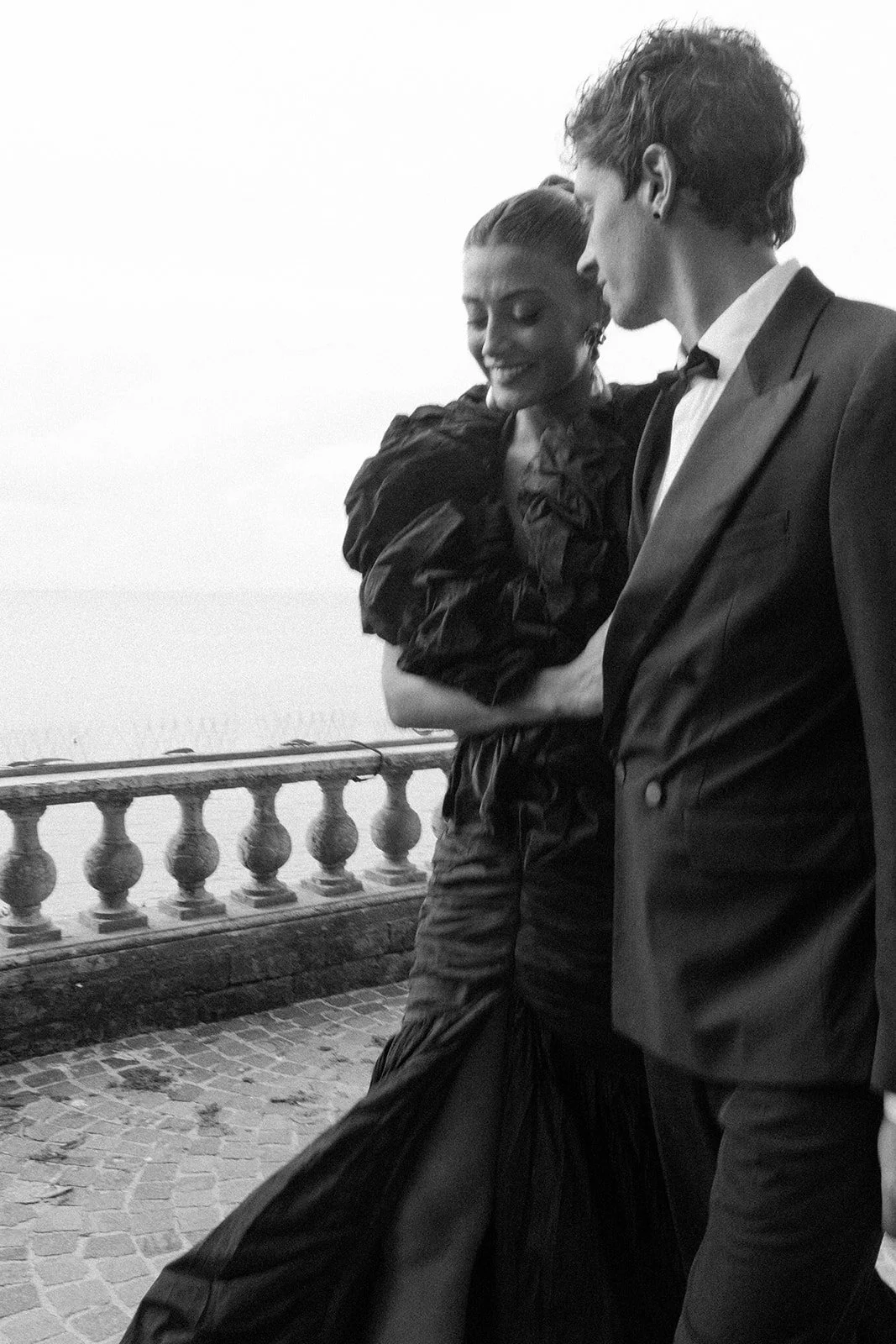  A black-and-white image with slight motion blur of the bride and groom walking toward the dinner reception. She’s wearing the same wedding gown, now striking in black. The movement feels fluid and cinematic, with a quiet intensity that makes the moment feel both timeless and bold. 