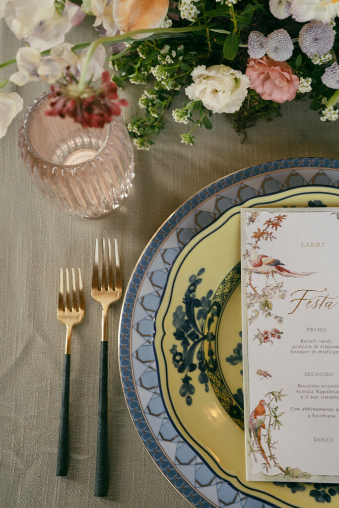 A Tuscany Wedding Styled at Villa Corsini: Timeless Editorial Inspiration in Italy Editorial wedding tablescape at Villa Corsini in Florence, Italy featuring floral arrangements, vintage patterned china, gold flatware, and an illustrated Italian menu.