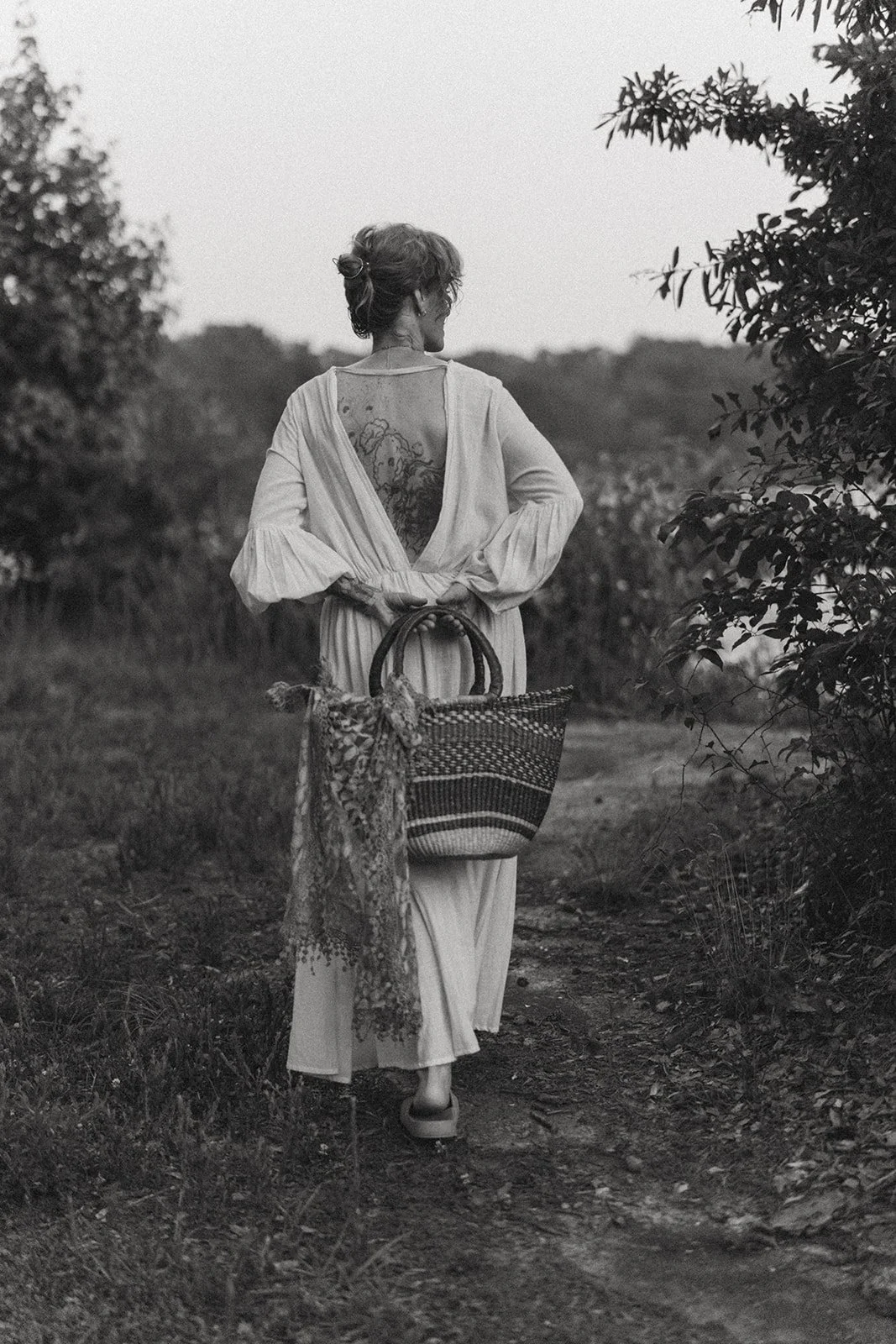  In one of my favorite quiet frames, Krystallin walks  down a soft path, the open back of her linen dress revealing her botanical tattoo — a subtle nod to the natural elements she works with. The woven basket, the wild stems, the softness of dusk… it all felt like a love letter to slow living. 