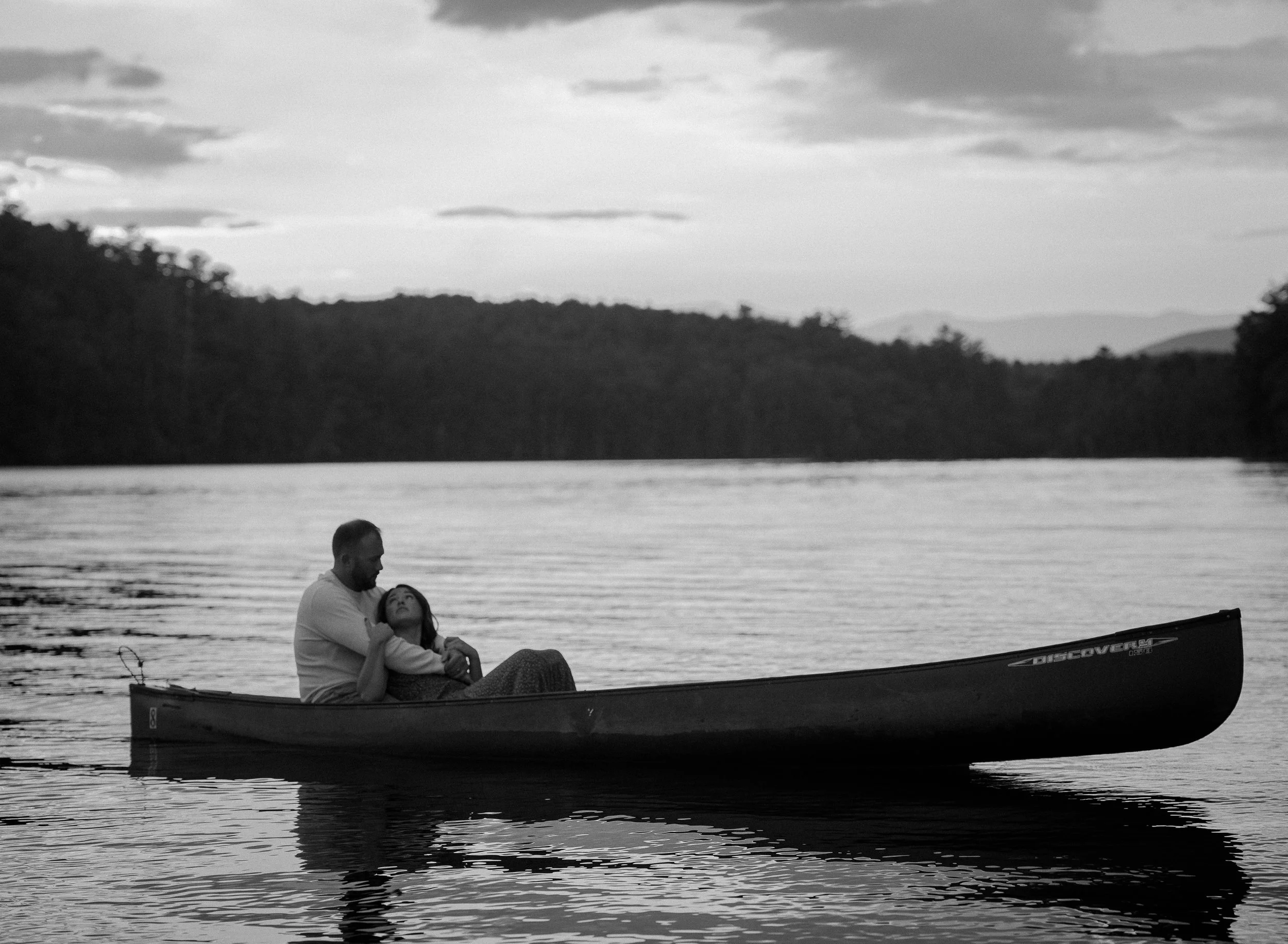 A couple sitting in a canoe on a lake at sunset, embracing each other.