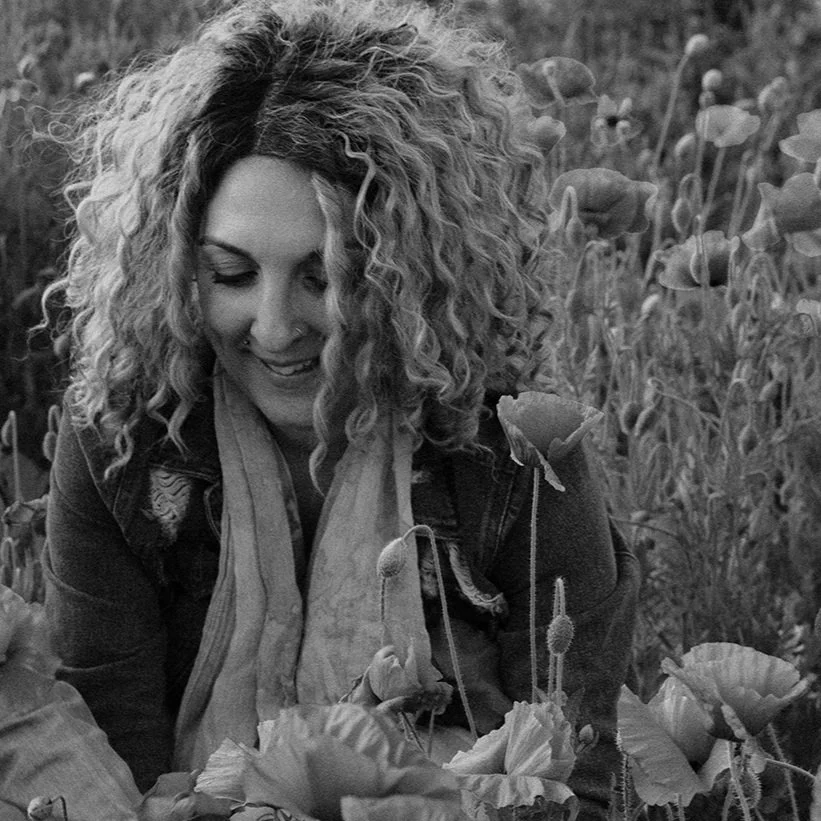 Black and white photo of a person with curly hair smiling in a field of flowers.