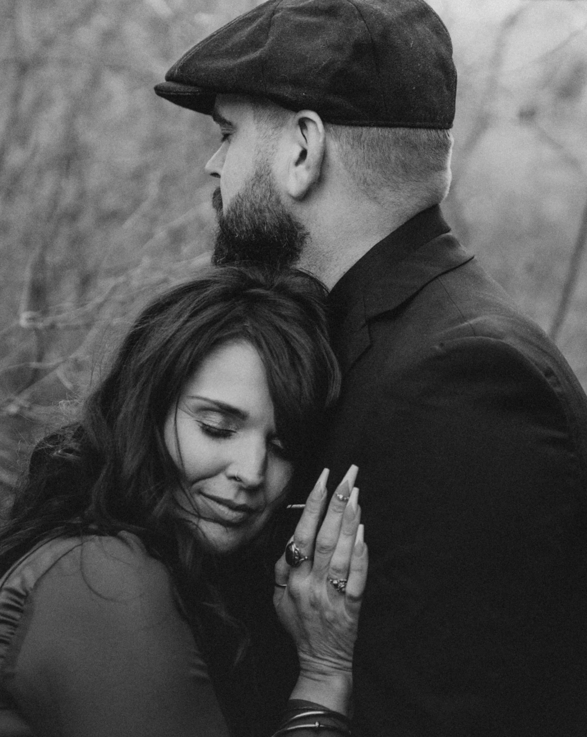 Black and white photo of a woman embracing a man wearing a flat cap, eyes closed, showing affection.
