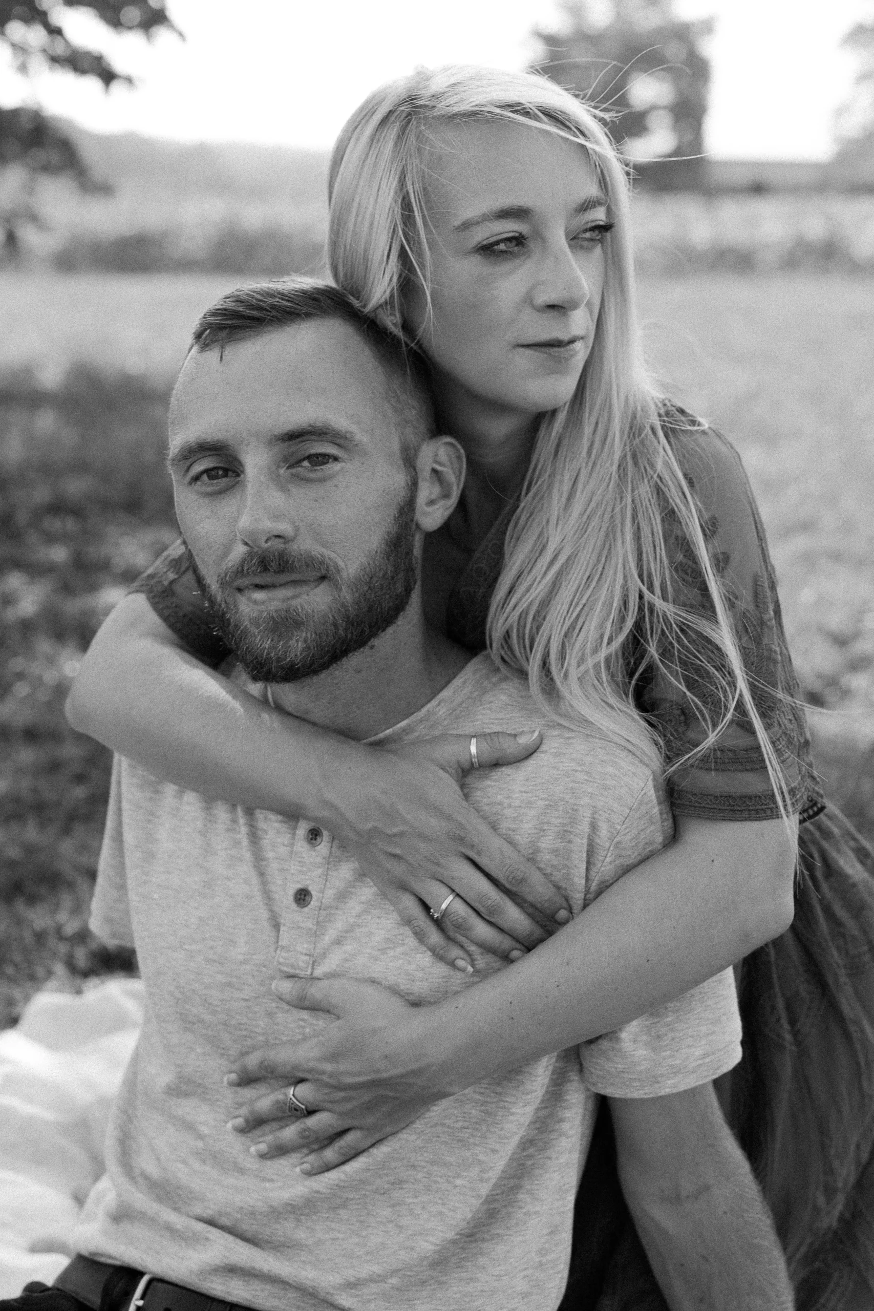 Black and white photo of a couple, with a woman leaning on a man, both looking to the side in an outdoor setting.