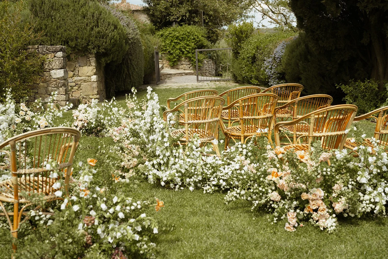 Outdoor garden ceremony setup with wicker chairs and floral arrangements on grass.