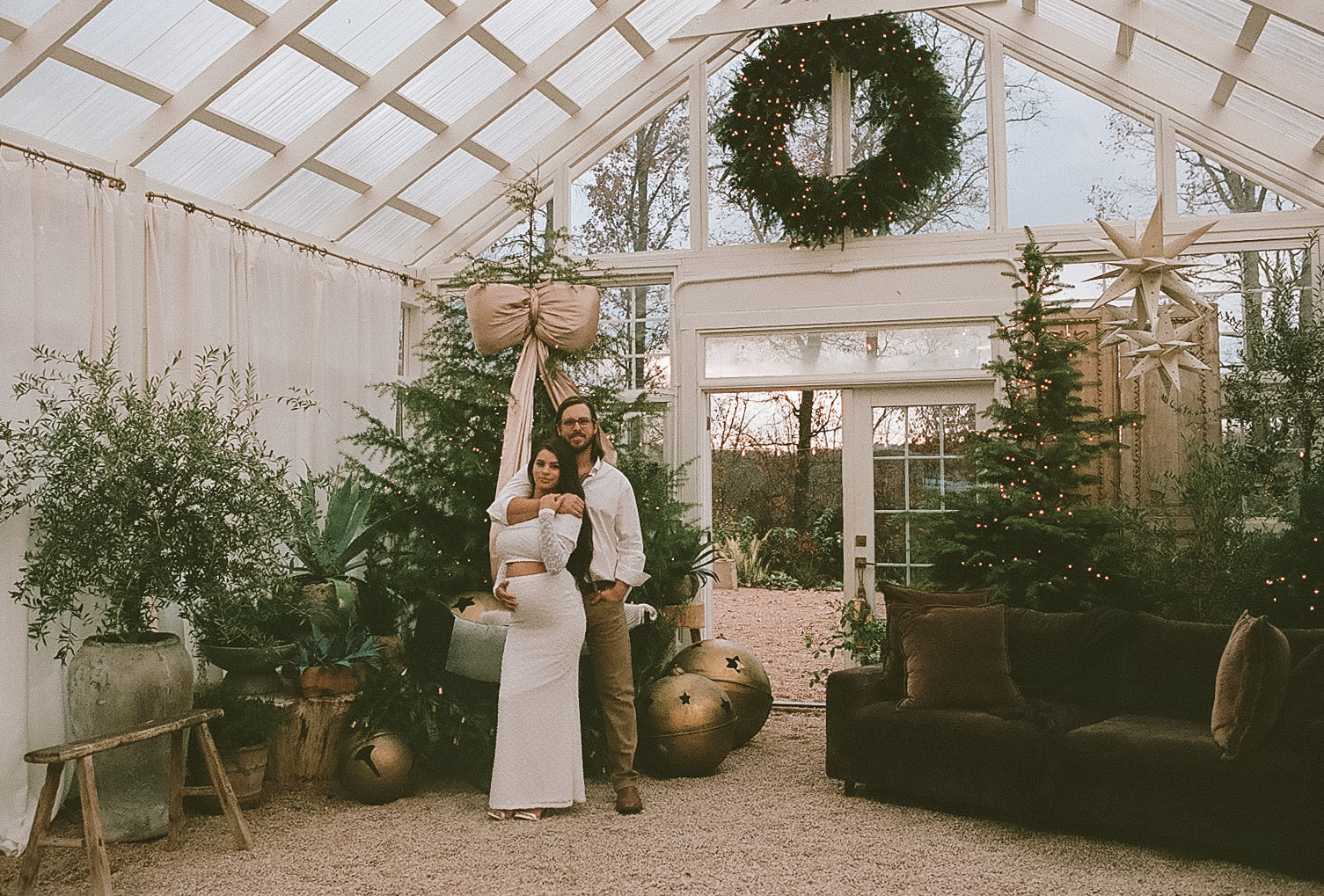 Couple standing together inside Fleurish Greenhouse in Charlotte, NC, surrounded by holiday greenery and soft natural light.