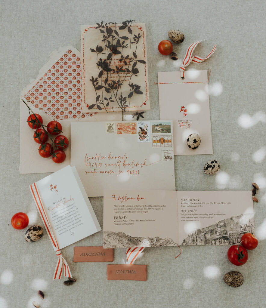 Editorial flat lay of Monteverdi Tuscany wedding paper goods with quail eggs, vine tomatoes, and vintage stamps styled on neutral linen.