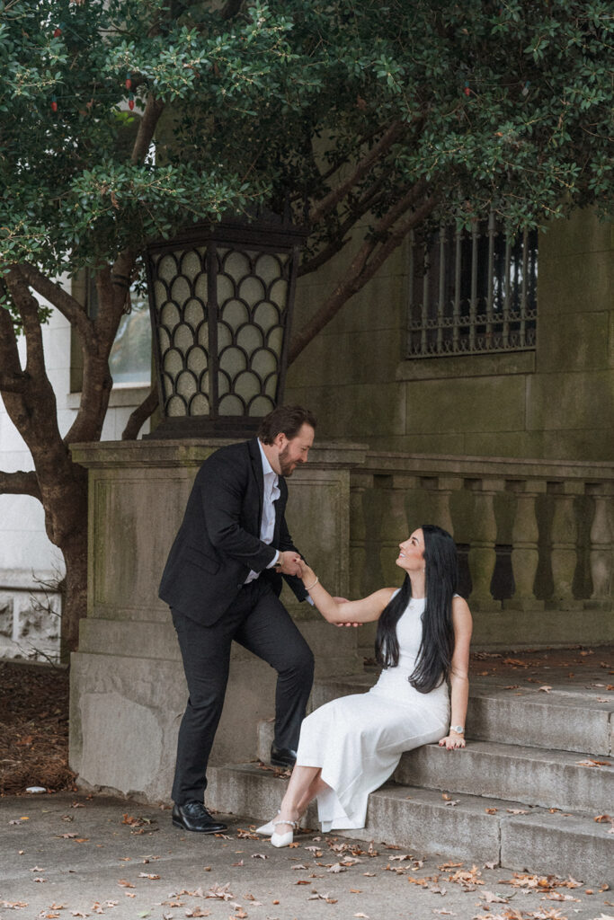 Couple sharing an intimate moment on the steps of a historic building, the man offering his hand to the woman as she looks up at him, captured during an editorial film session near Charlotte.