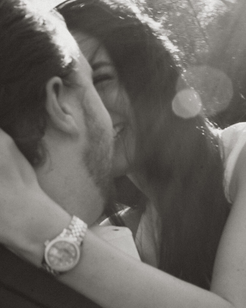 Intimate black-and-white close-up of a couple laughing and leaning in for a kiss in soft afternoon light, captured in a cinematic editorial style in Charlotte.