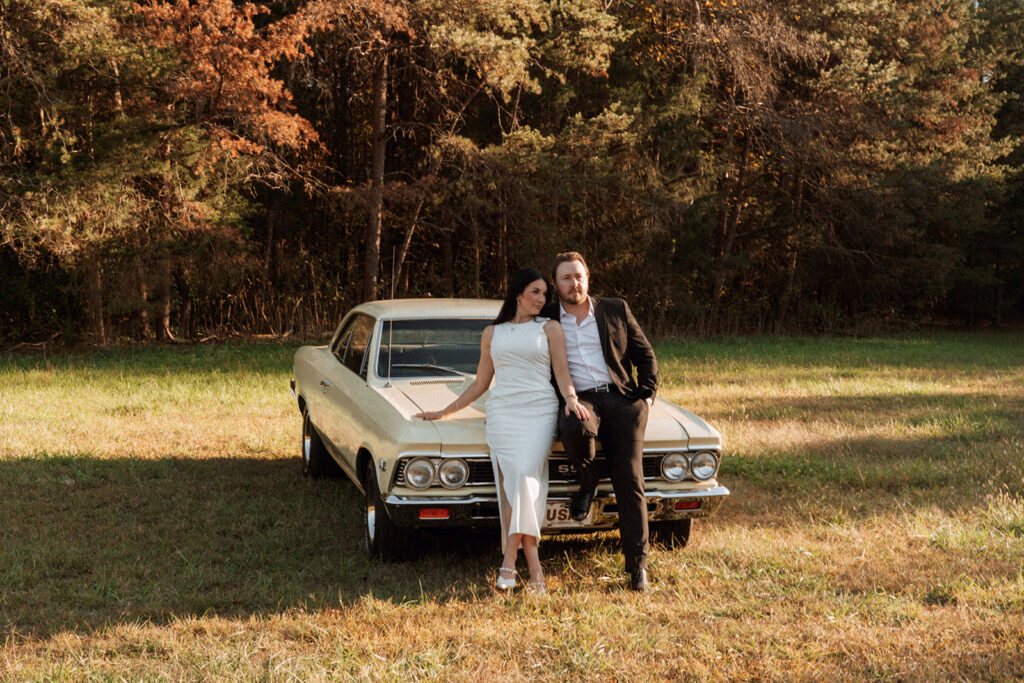 Couple leaning against a pale yellow vintage Chevelle in a sunlit open field, captured during an editorial couples session near Charlotte with timeless film-inspired tones.