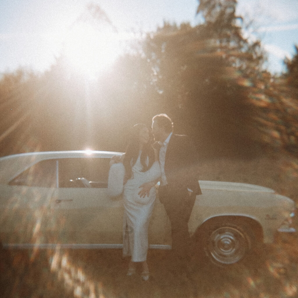 Couple standing beside a pale yellow vintage Chevelle in soft golden light, captured in cinematic film style during an editorial couples session near Charlotte.