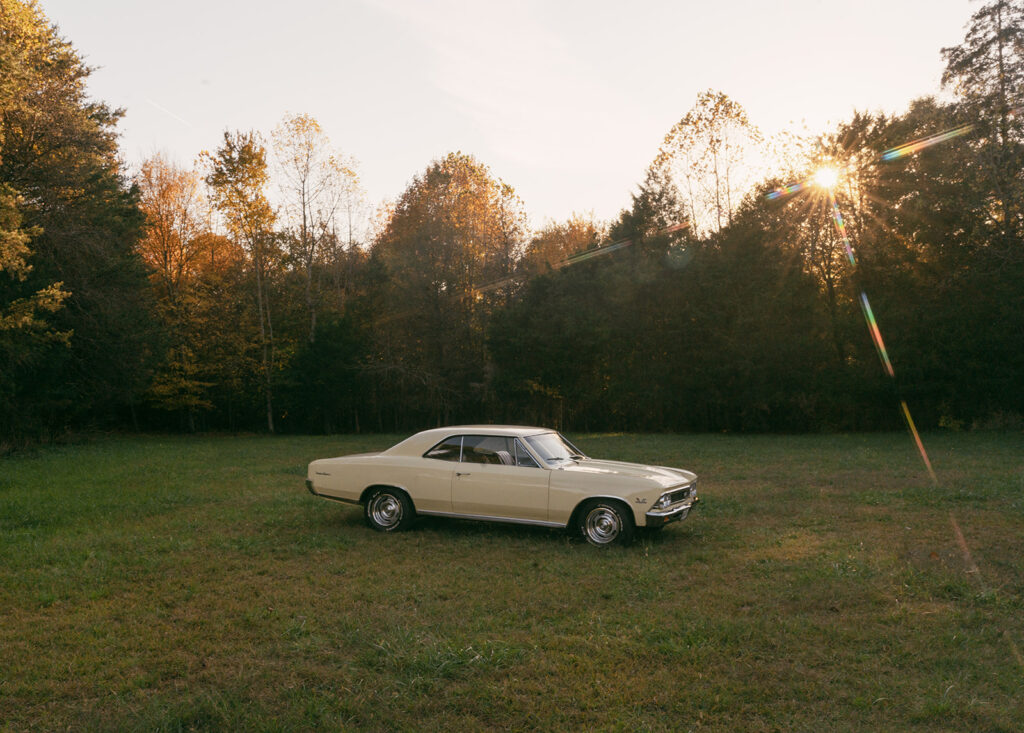 Vintage cream Chevelle parked in an open field at sunset, surrounded by golden trees during an editorial couples session near Charlotte.