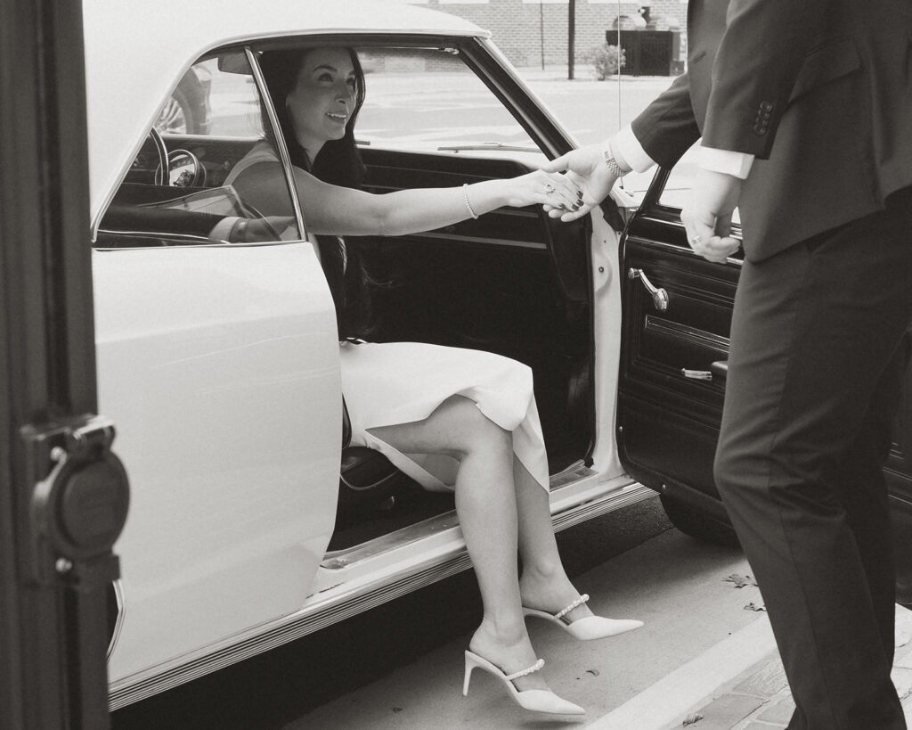 Woman stepping out of a vintage white car, reaching for her partner’s hand, captured in timeless black and white during an editorial couples session in Charlotte.