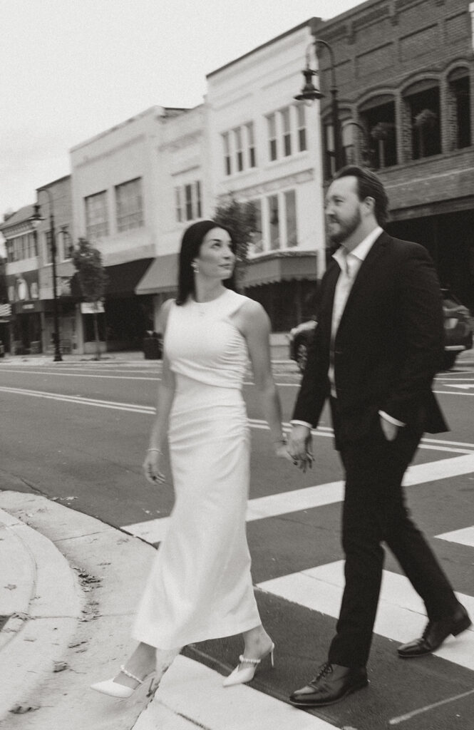 Couple walking hand in hand across a downtown street, captured in motion during an editorial film photography session near Charlotte.