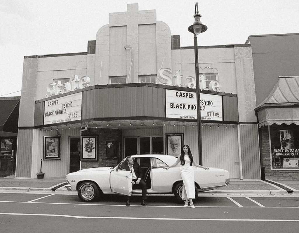 Couple posing with a pale yellow Chevelle in front of the historic State Theater in downtown Charlotte.