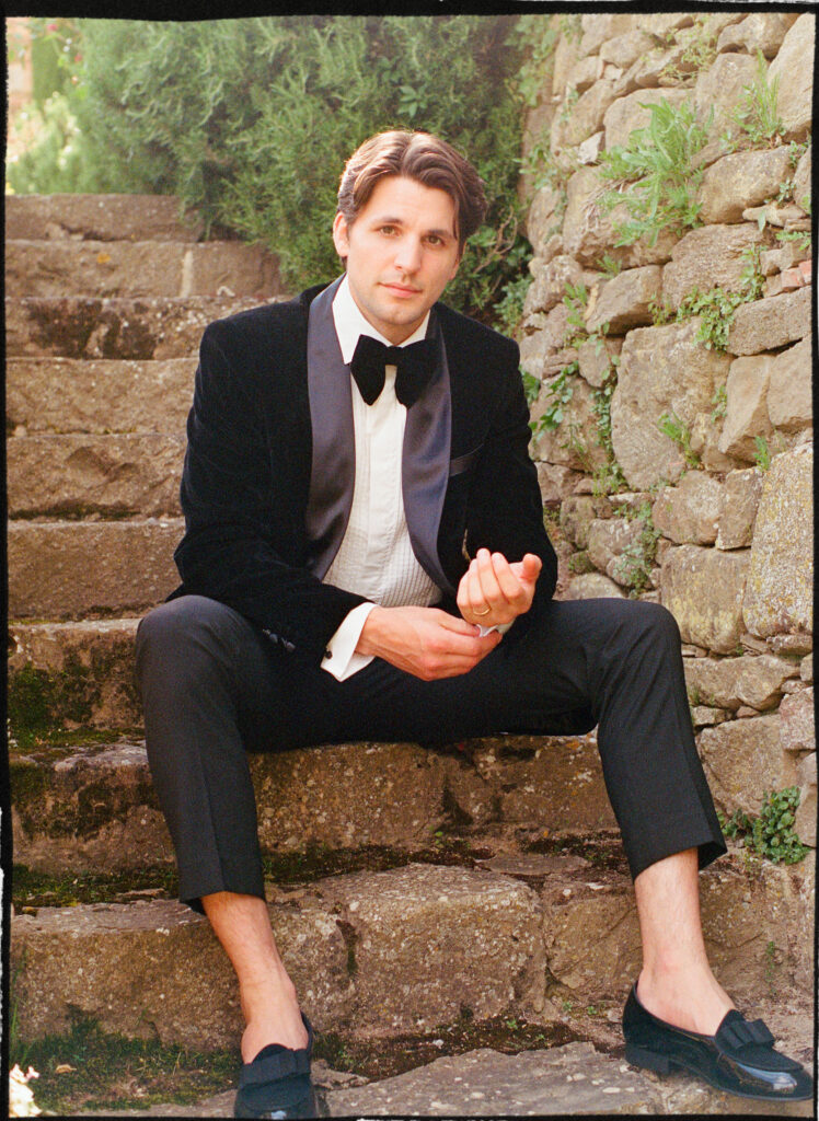 A Timeless Monteverdi Tuscany Wedding Groom portrait on stone staircase at Monteverdi Tuscany in black tuxedo