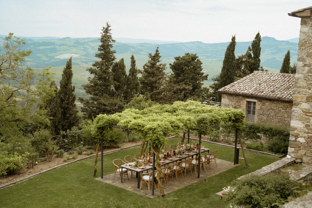 Outdoor reception table under a wisteria canopy at Monteverdi Tuscany with panoramic views of Val d’Orcia’s rolling hills.