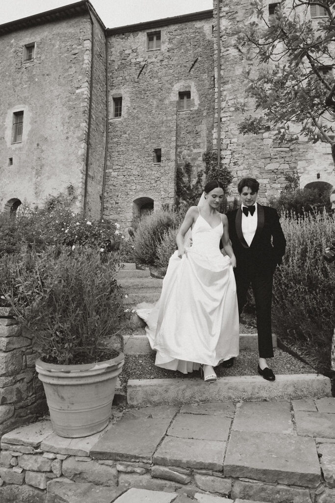 Bride in Danielle Frankel gown and Jane Rhyan The Collection veil walking with groom in black velvet tuxedo through Monteverdi Tuscany.