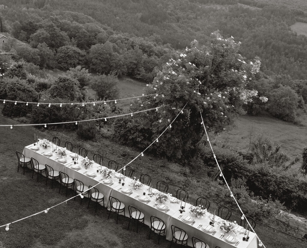 Black-and-white aerial view of a long dinner table under string lights overlooking the hills at Monteverdi Tuscany.