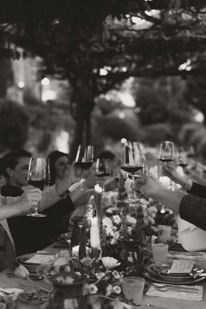 Black and white photo of guests raising wine glasses in a toast during an outdoor dinner at Monteverdi Tuscany.