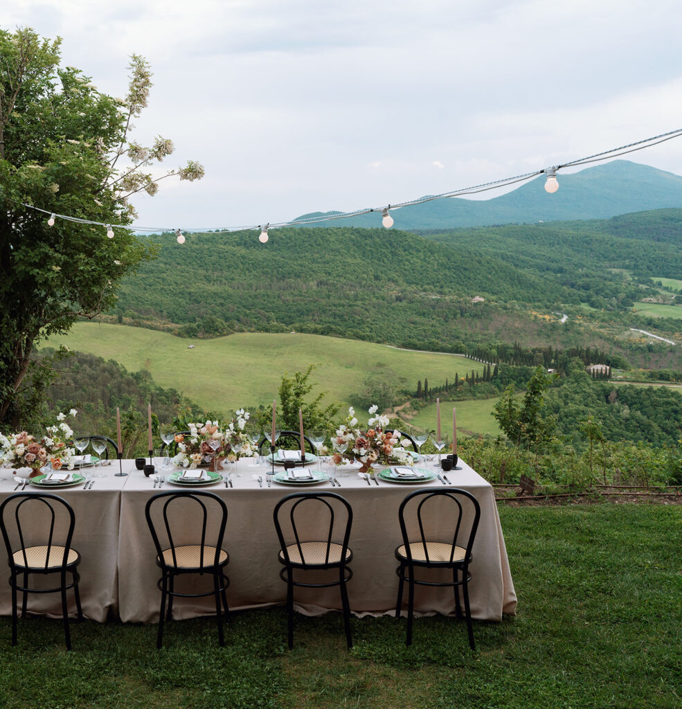 Elegant outdoor dinner table under string lights at Monteverdi Tuscany overlooking the Val d’Orcia hills.