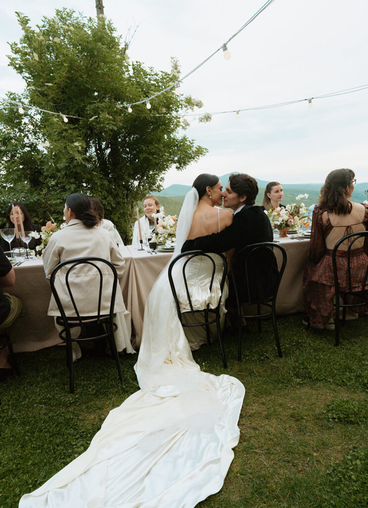 Bride and groom share a kiss during dinner surrounded by guests at Monteverdi Tuscany.