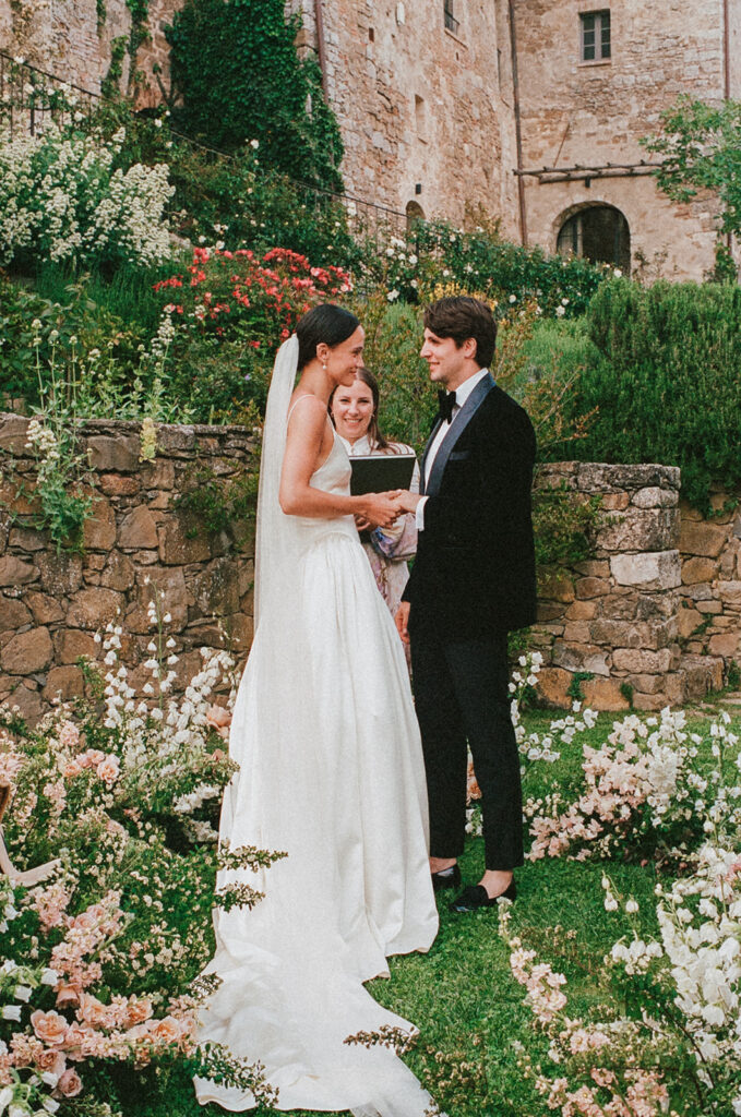 Bride in Danielle Frankel gown and Jane Rhyan The Collection veil exchanging vows with groom in black velvet tuxedo at Monteverdi Tuscany.