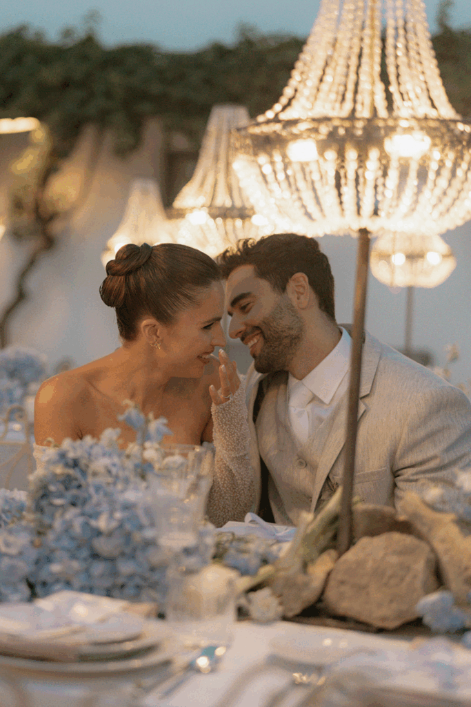 Bride and groom leaning in together at an intimate candlelit wedding dinner, sharing a quiet, unposed moment