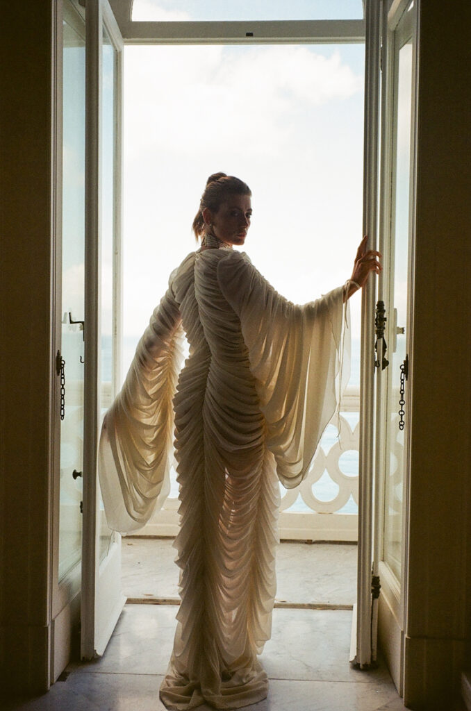 Why Luxury Wedding Photography Is About Trust, Not Shot Lists Bride standing in soft light near an open window wearing an editorial wedding gown, photographed in a quiet, candid moment
